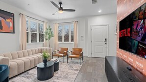 Un salon moderne comprenant un canapé, deux fauteuils, une table basse et un téléviseur fixé au mur.