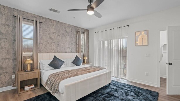 Une chambre à coucher avec un lit, une table de chevet, un ventilateur de plafond et une fenêtre avec des rideaux.