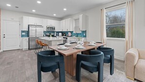 Une cuisine moderne avec des meubles blancs, un îlot central et un coin repas doté de chaises foncées.