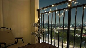Een balkon met uitzicht op een stadsbeeld 's nachts, met lichtslingers en een potplant.