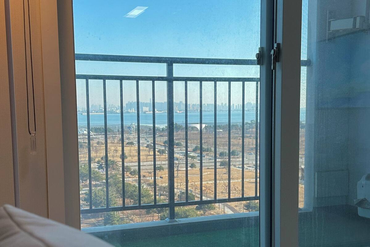 A bedroom with a large window overlooking a cityscape and a body of water.