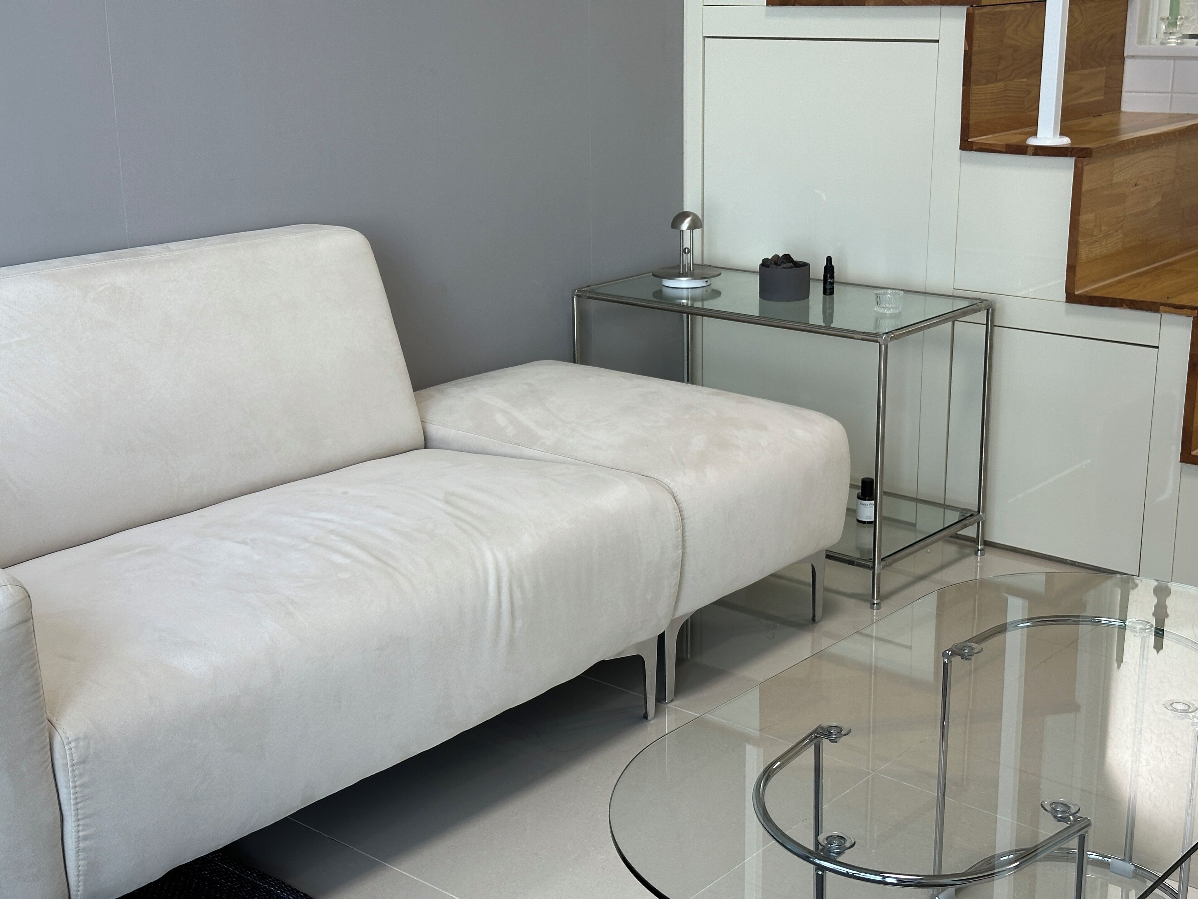 A modern living room with a white leather sofa, a glass coffee table, and a small side table with a lamp.