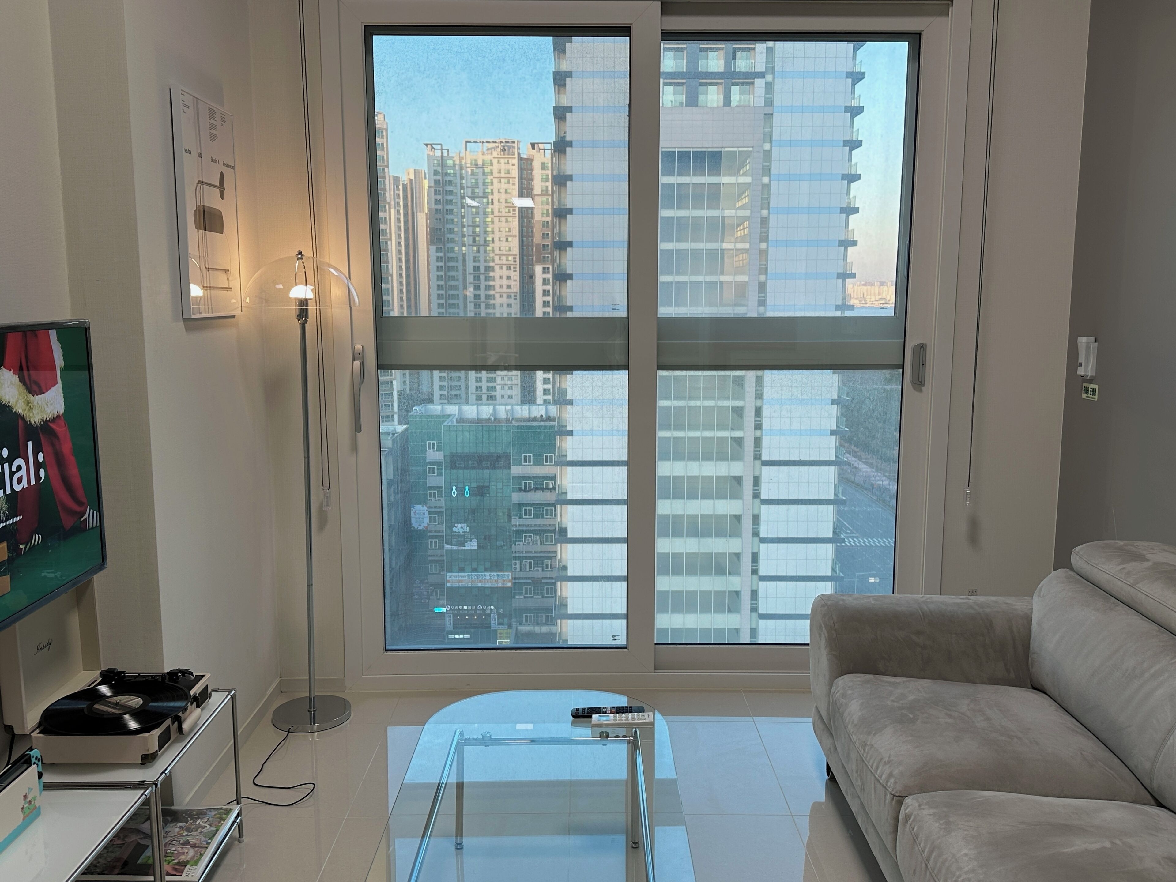 Una sala de estar moderna con un ventanal grande, un sofá, una mesa de centro y un televisor sobre un mueble.