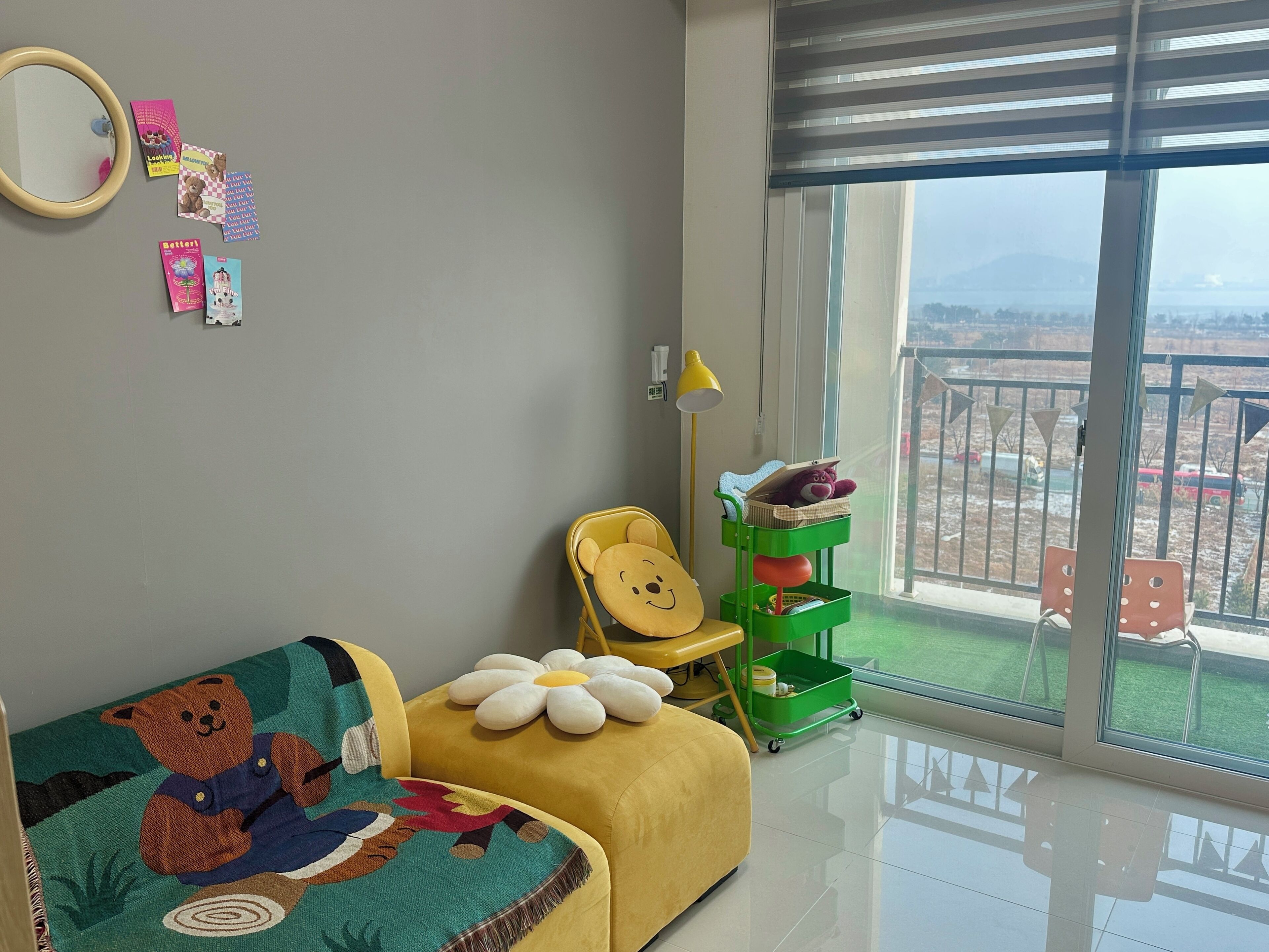 A child’s room with a sofa, a green toy storage cart, and a view of a snowy landscape through a large window.