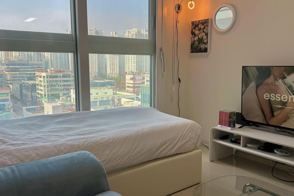 A modern hotel room with a large bed, a TV, and a view of the cityscape.
