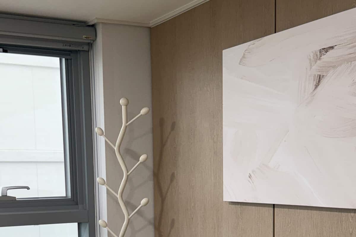 A room with a wooden floor, a white wall with a textured pattern, a window with a white blind, and a white floor lamp.