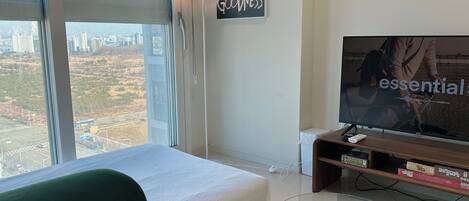 Een hotelkamer met een bed, een televisie, een lamp en uitzicht op de stad.