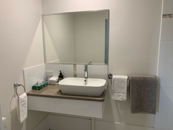 Un baño con lavamanos blanco, un espejo y un perchero para toallas.