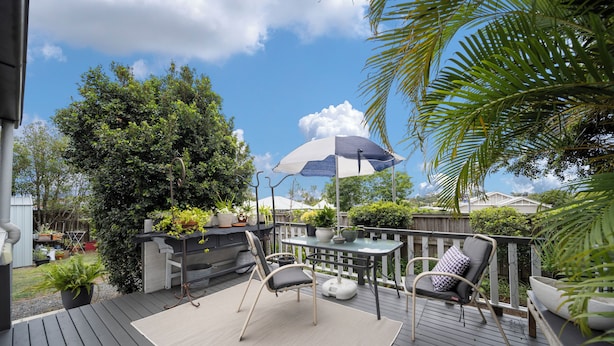 A deck with a table and chairs, surrounded by potted plants and a large umbrella. - Verandah Motel (Gympie)