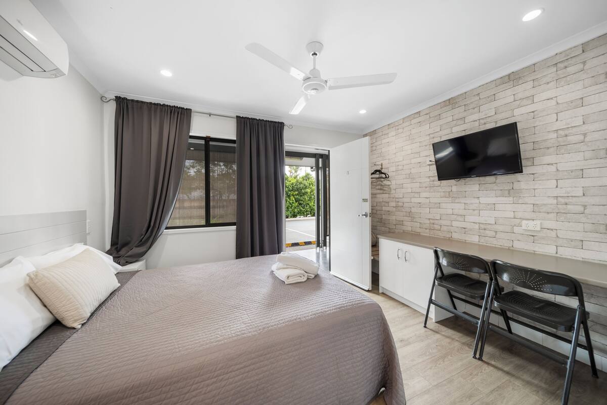 Ein modernes Hotelzimmer mit Bett, Schreibtisch, Sessel, Fernseher und Balkon.