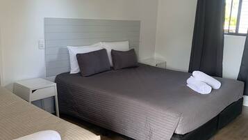 Ein modernes Schlafzimmer mit einem großen Bett, einer kleinen Sitzecke, einem Nachttisch, einem Deckenventilator und einem Fenster mit Vorhängen.