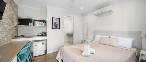 A modern hotel room with a bed, a desk, a chair, and a small kitchenette.