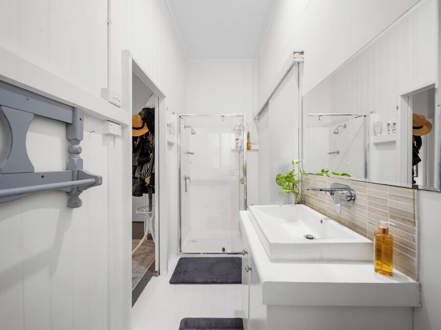 Een smalle badkamer met een wit wastafel, een grote spiegel en een douchehoek.