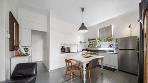 A modern kitchen with white cabinetry, a dining table with chairs, a black leather bench, and a refrigerator. - Verandah Motel (Gympie)