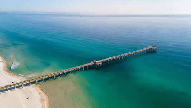 An aerial view of a long pier extending into the ocean, with clear water and a sandy beach on one side. - August Sale - Private Pool –Gameroom - blk 2 beach (Panama City)