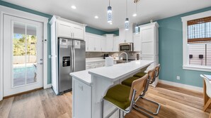 A modern kitchen with white cabinets, a stainless steel refrigerator, a microwave, and a bar area with stools. - August Sale - Private Pool –Gameroom - blk 2 beach (Panama City)