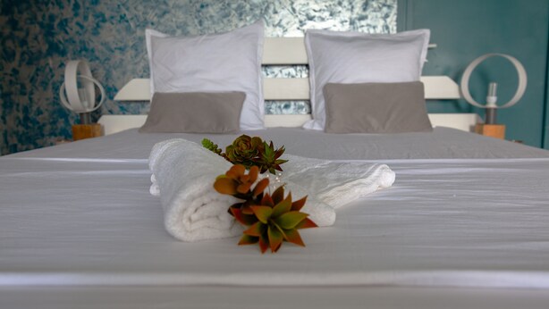 A neatly made bed with white linens and a folded towel with green and brown plants. - Enjoy the peace and quiet of nature in this fresh, bright villa. (Saint-Joseph)