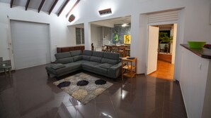 A spacious living room with a sectional sofa, a dining area with a table and chairs, and a kitchen visible through an open doorway. - Enjoy the peace and quiet of nature in this fresh, bright villa. (Saint-Joseph)