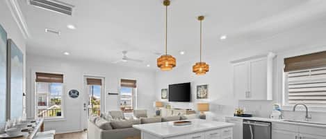 A modern kitchen with white cabinetry, a central island, pendant lighting, and a dining area with bar stools.