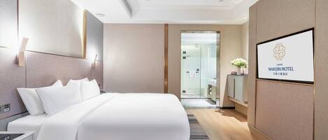 A modern hotel room with a large bed, a bedside table, a nightstand, a mirror, and a framed logo on the wall.