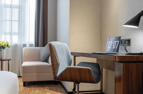 Une chambre d’hôtel équipée d’un canapé, d’un bureau avec un ordinateur portable, d’une lampe et d’une horloge murale.