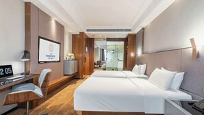 Ein modernes Hotelzimmer mit einem großen Bett, einem Schreibtisch und einem Sessel. An der Wand befindet sich ein Fernseher und ein Schild mit der Aufschrift 'Wanjin Hotel'.