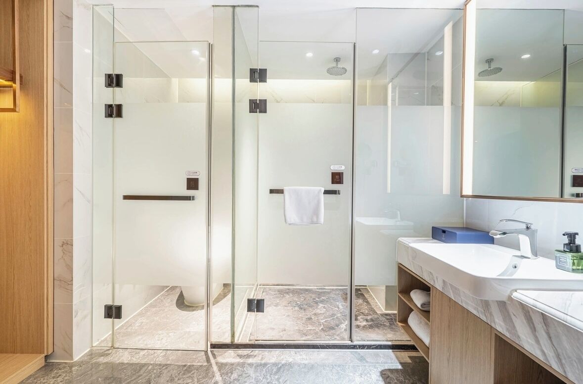 Un baño moderno con ducha envuelta en vidrio, un lavabo blanco y un espejo grande.