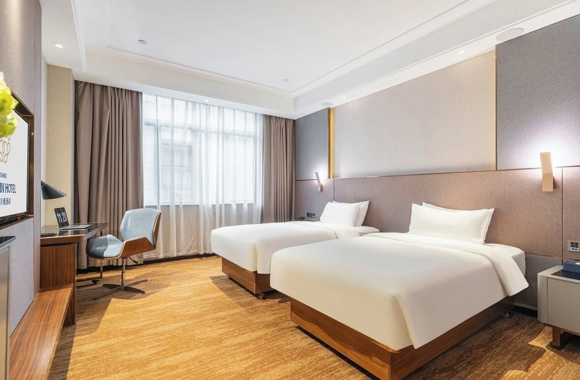 Une chambre d’hôtel avec deux lits, un bureau avec une chaise, une table de chevet et une grande fenêtre avec des rideaux.