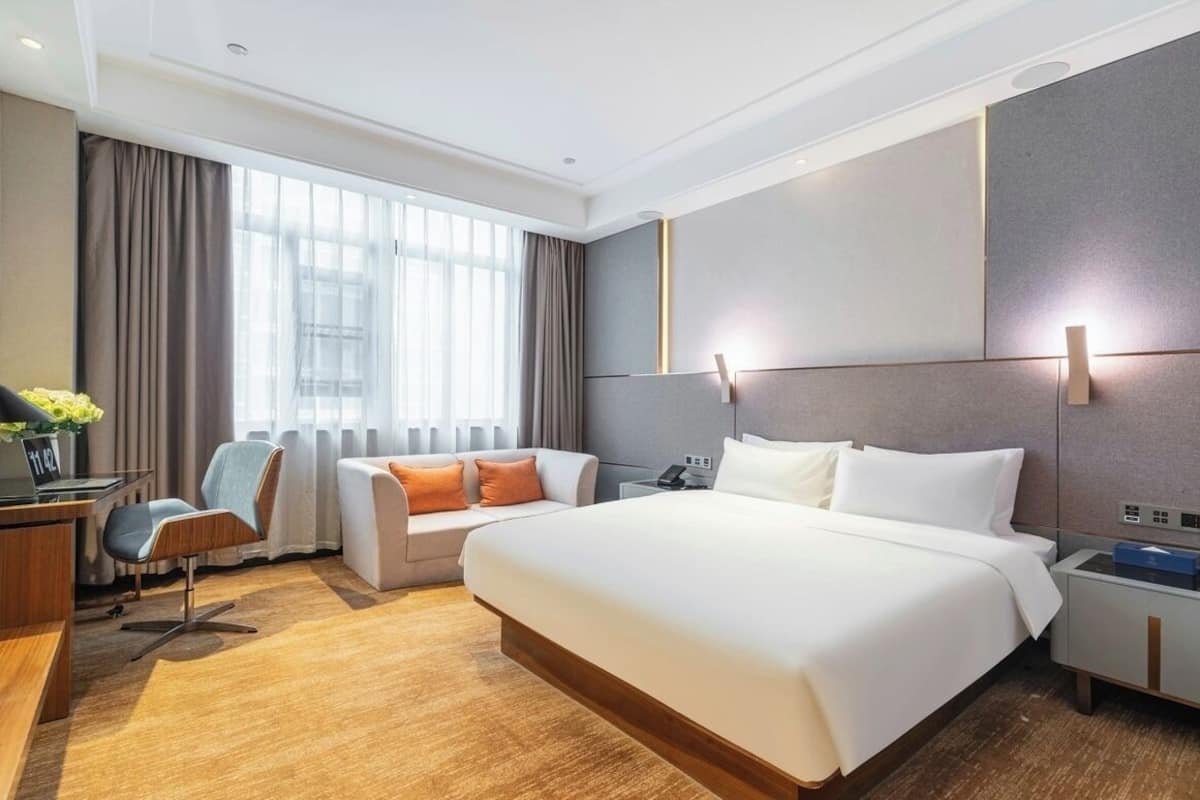 A modern hotel room with a large bed, a sofa, a desk, and a nightstand.