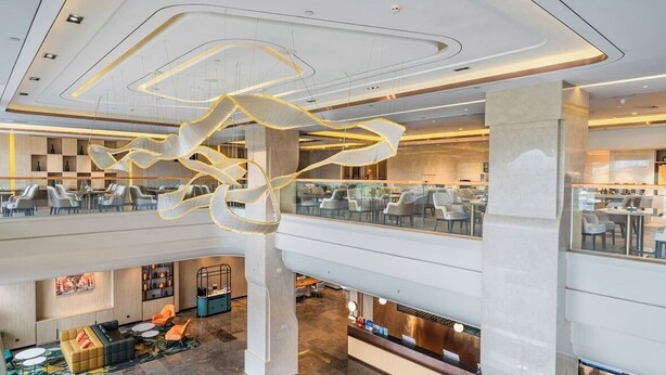 Eine moderne Hotelhalle mit großzügiger Sitzecke, einer zentralen dekorativen Lichtinstallation und Blick auf die Ebene darunter.