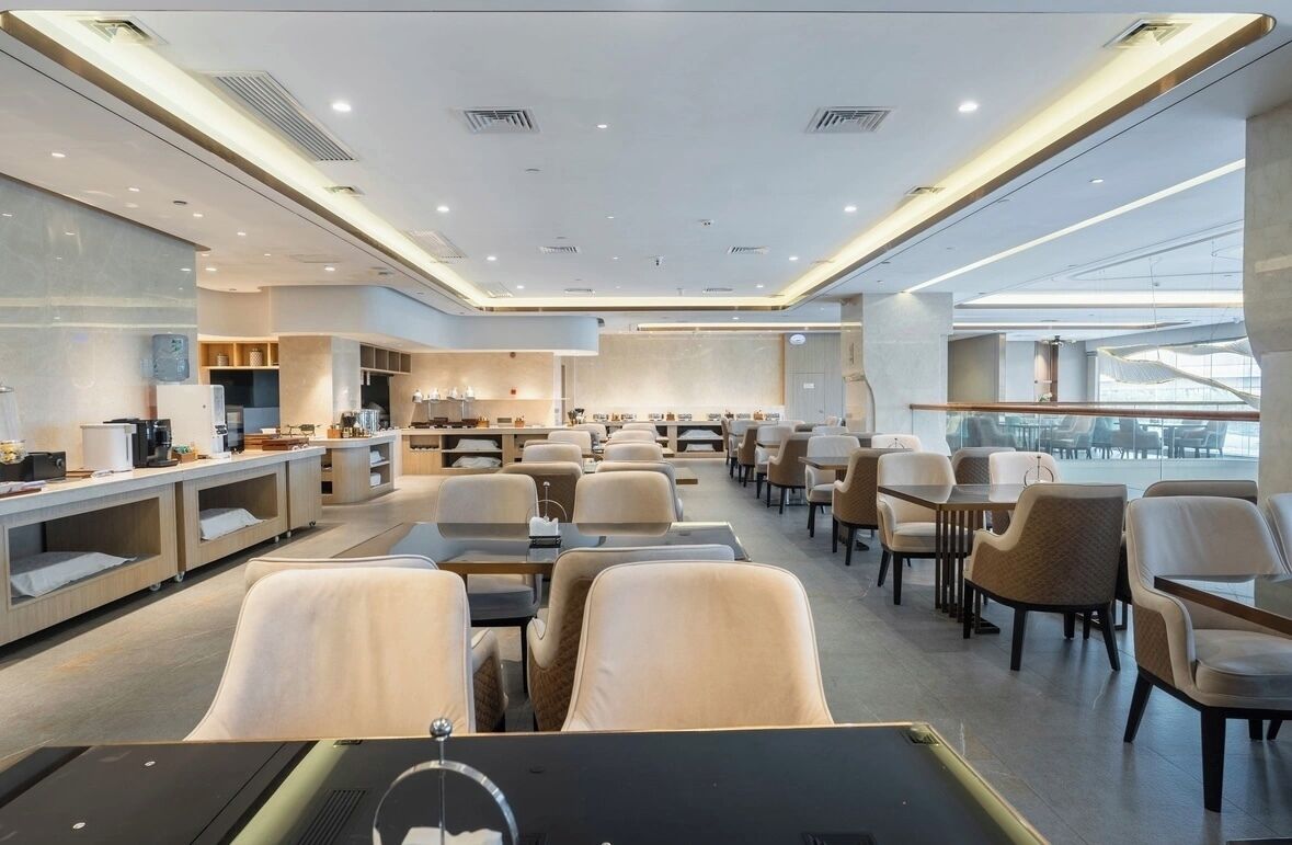 A modern hotel lobby with a spacious seating area, a kitchenette, and a large window providing a view of the city.