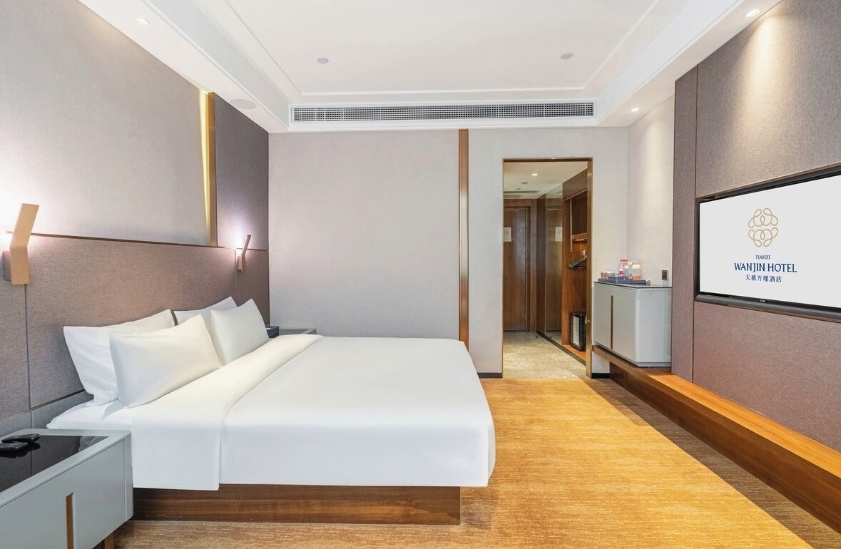 A hotel room with a bed, bedside table, and a TV screen displaying the hotel name.