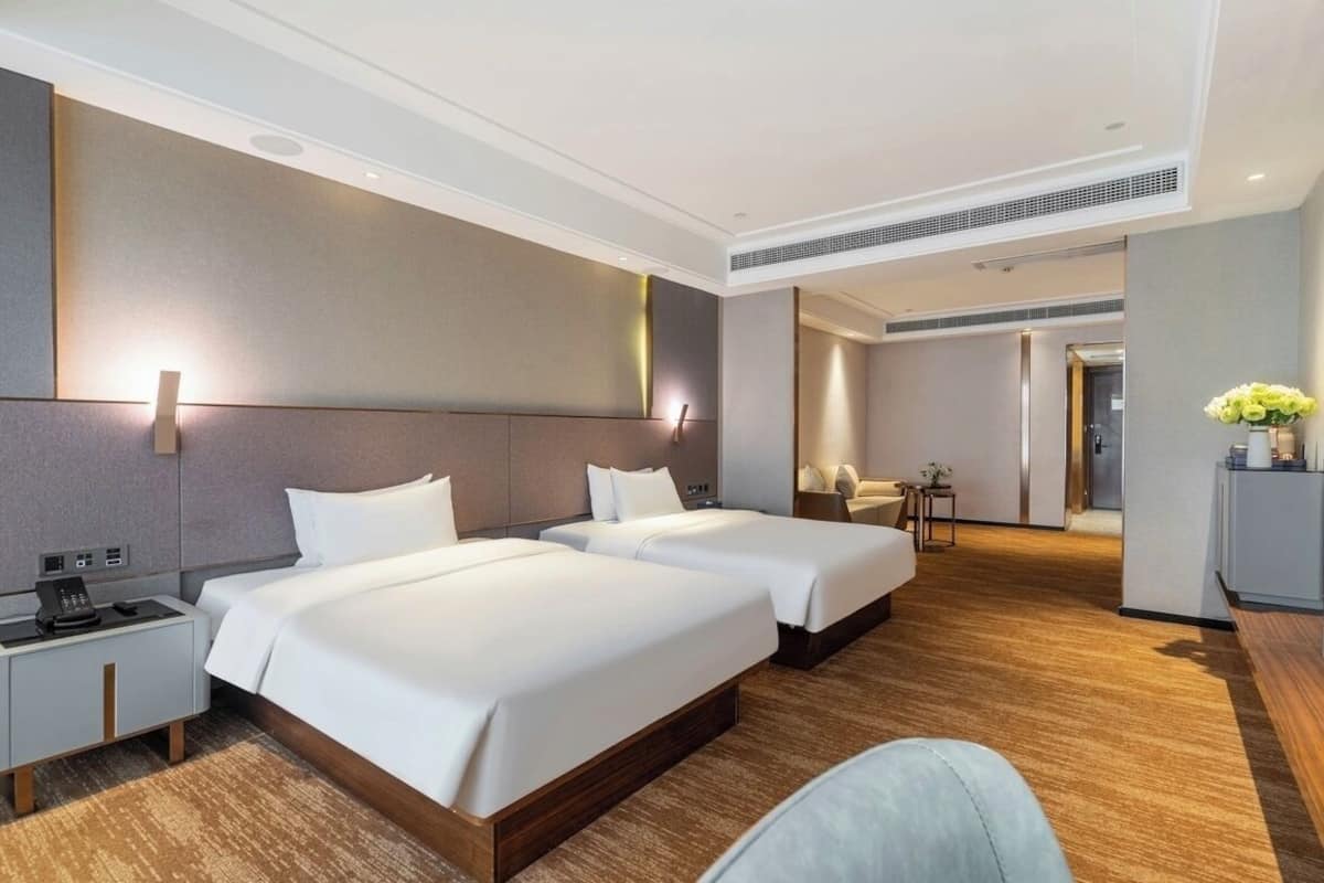 A hotel room with two beds, a desk, a chair, a small table, and a mirror.