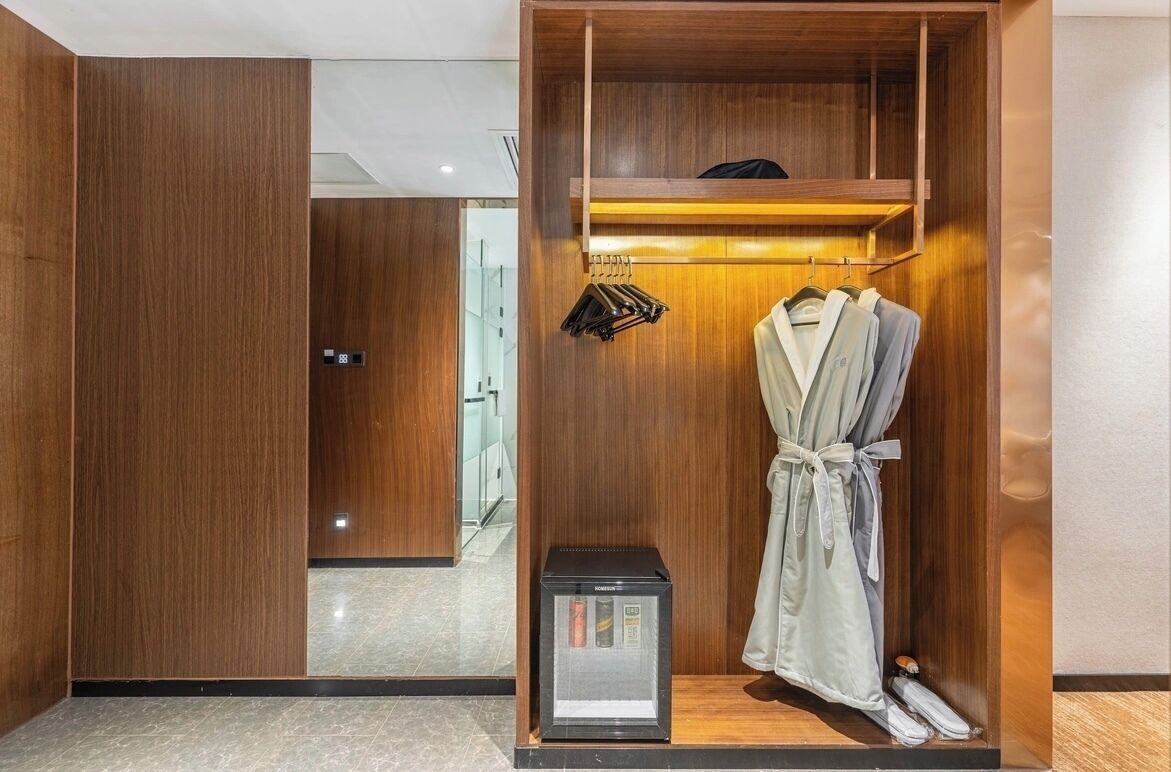 A wooden wardrobe with a robe hanging inside, a small black appliance, and a mirror.