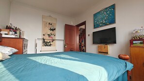 A bedroom with a bed, a TV, a wooden cabinet, a painting, and a door leading to another room. - Mommy's home with breadfast and more (Qingdao)