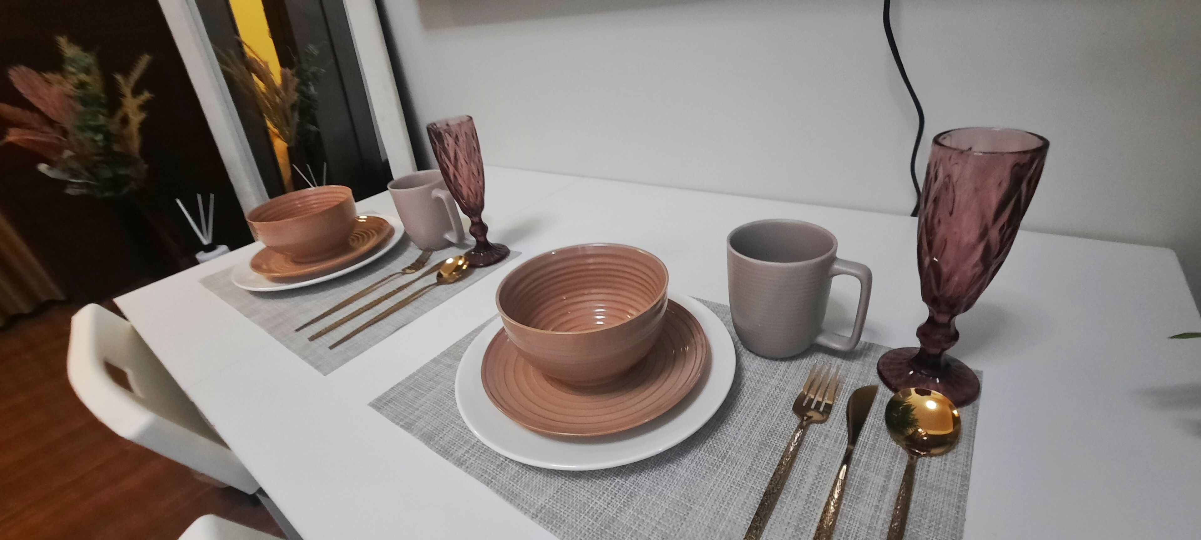 A dining table set with brown bowls, a gray mug, and gold cutlery.