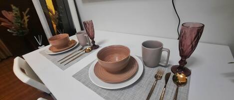A dining table set with brown bowls, a gray mug, and gold cutlery.