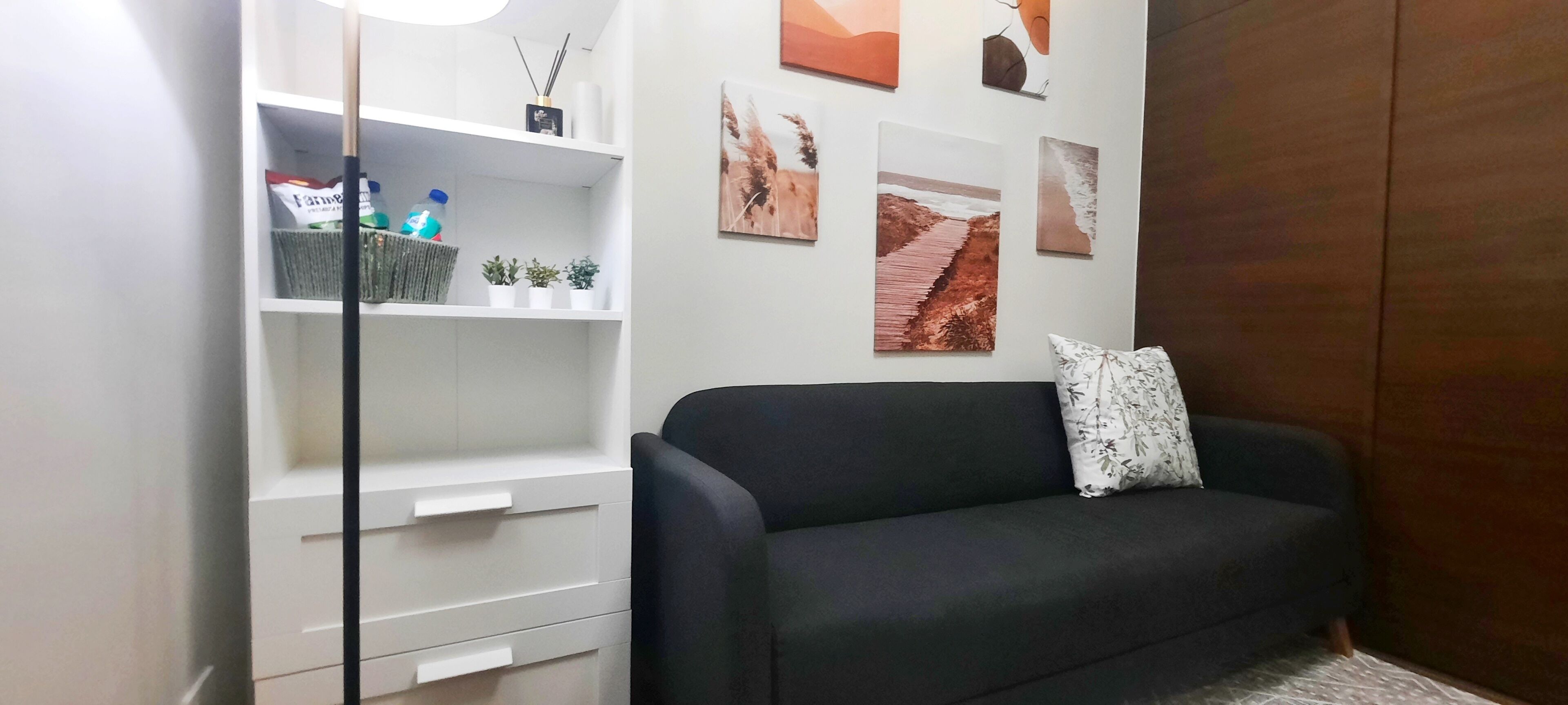 A modern living room with a black sofa and white storage unit against a white wall.