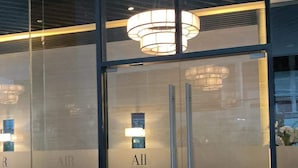 Ein moderner Hotelaufgang mit Glastüren, einem zentralen Kronleuchter und einem sichtbaren Empfangsbereich.