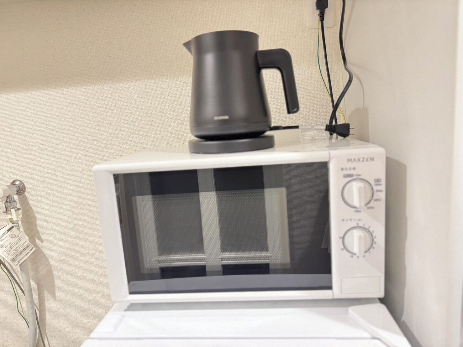 Un microondas con una olla negra encima, conectado a un enchufe en una pared blanca.