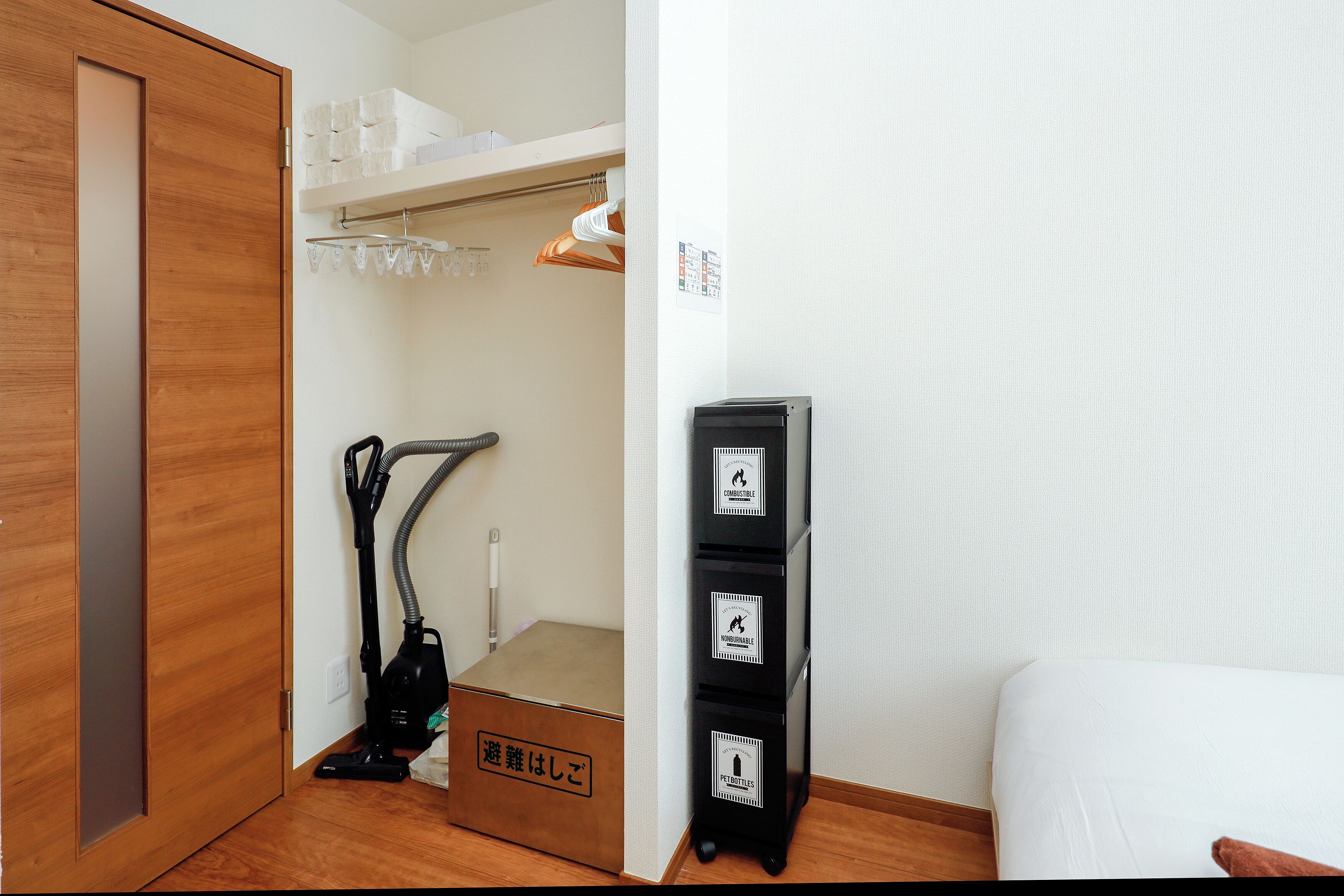 Habitación de hotel con piso de madera, una cama, un aspirador y un armario con cajones etiquetados.