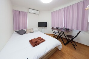 A bedroom with a bed, a desk, a chair, a flat-screen TV, and purple curtains. - Zenith Garden TOGOSHI (Tokyo)