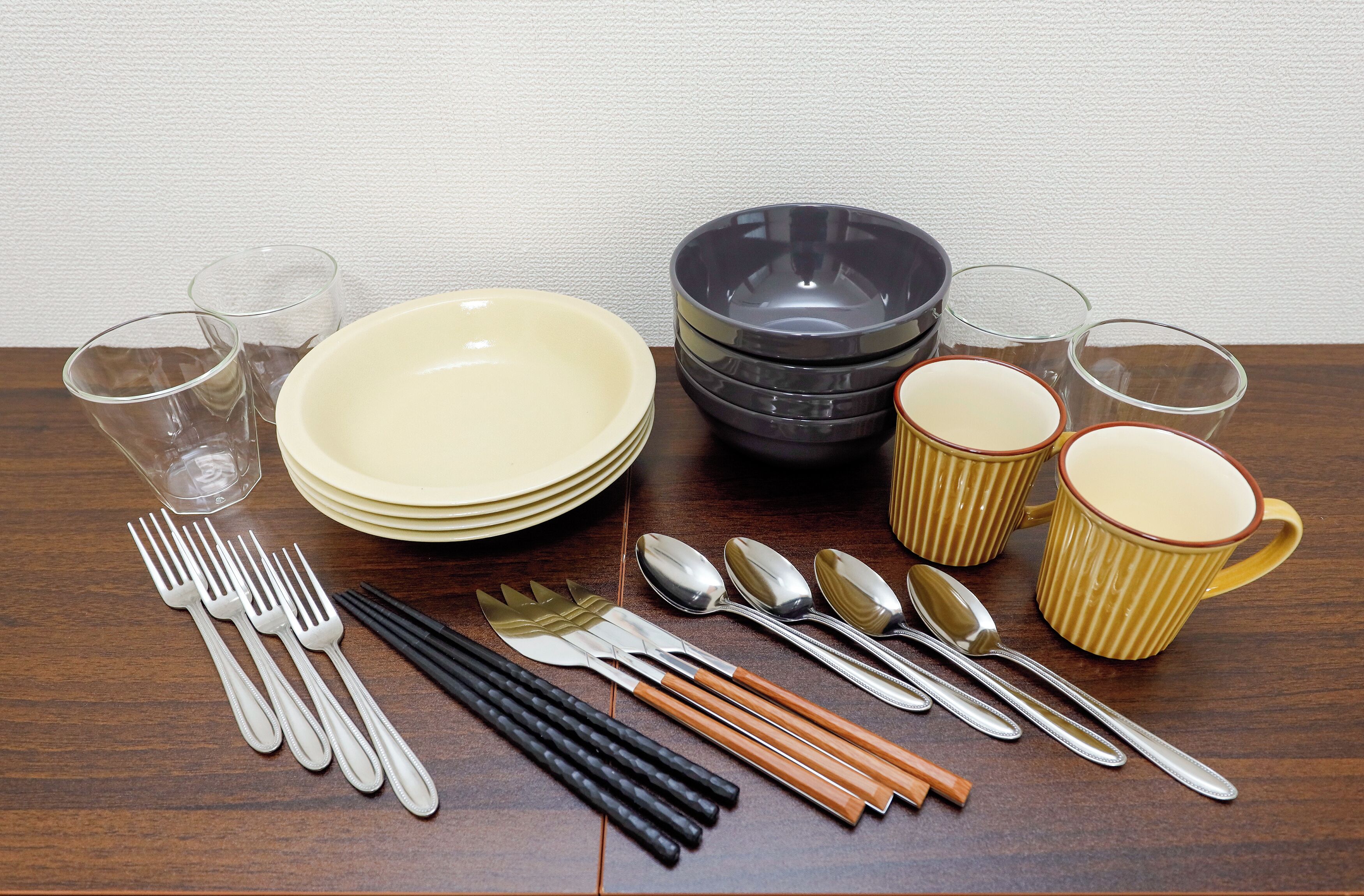 A dining set with plates, bowls, cups, cutlery, and chopsticks arranged on a wooden table.