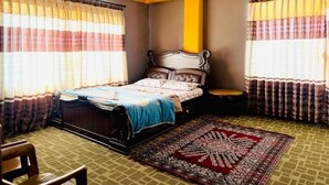 Een slaapkamer met een bed, gordijnen, een vloerkleed en een stoel.