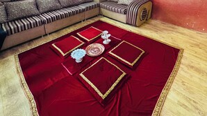 Een woonkamer met een hoekbank, een rood tapijt en een klok aan de muur.