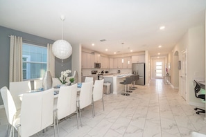 A modern kitchen with white cabinets, a central island, and a dining area with white chairs and a chandelier.