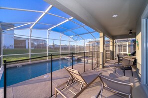 A covered outdoor pool area with lounge chairs and a barbecue setup.