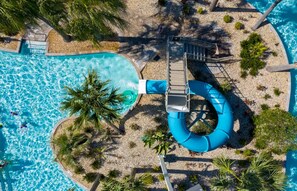Vista aérea de un área de piscina con tobogán de agua, palmeras y un sendero de piedra.
