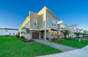 A modern two-story residential building with a garage, a covered driveway, and a well-maintained lawn.