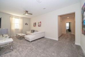 A spacious living room with a white sofa, a glass coffee table, and a ceiling fan. There is a door leading to another room. - Pretty Villa 6Bed/5Bath/Pool/Jacuzzi/18Min Disney (Davenport)
